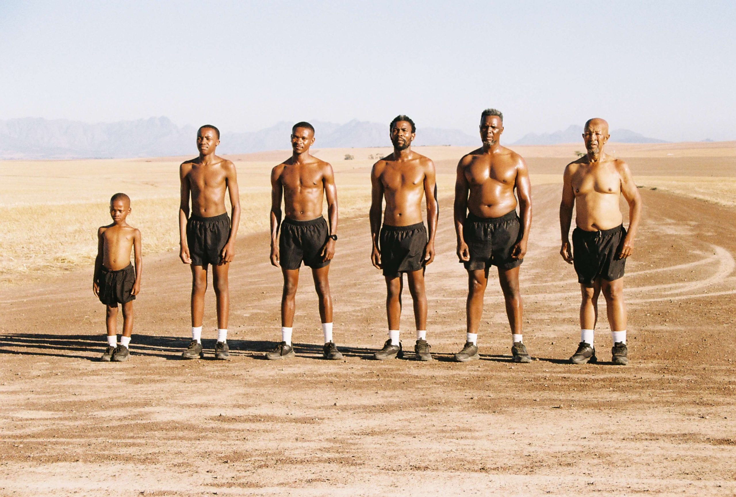 Image of 6 men at different ages standing in a line in the desert.